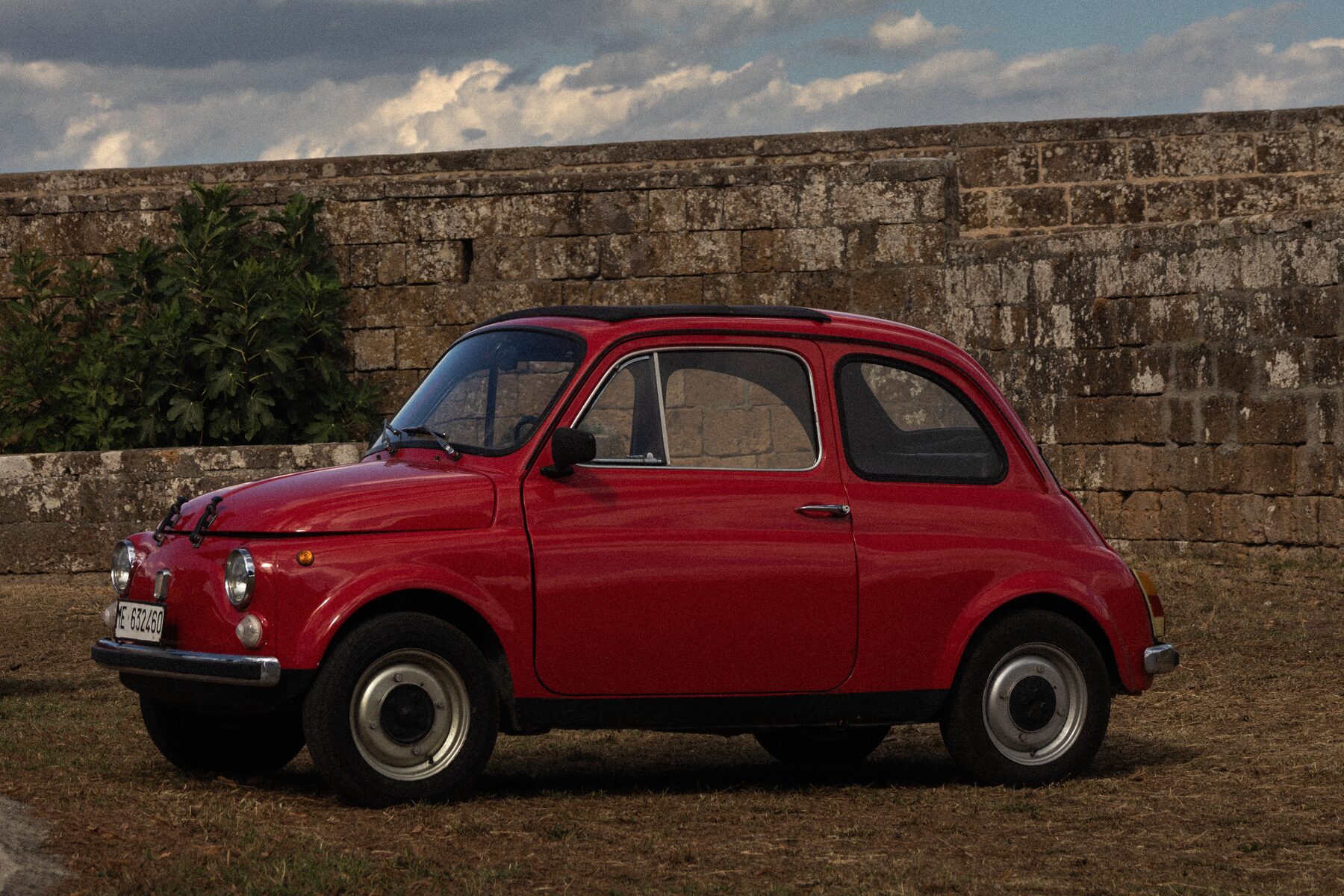 Vintage red Fiat 500 parked beside an old stone fortress wall