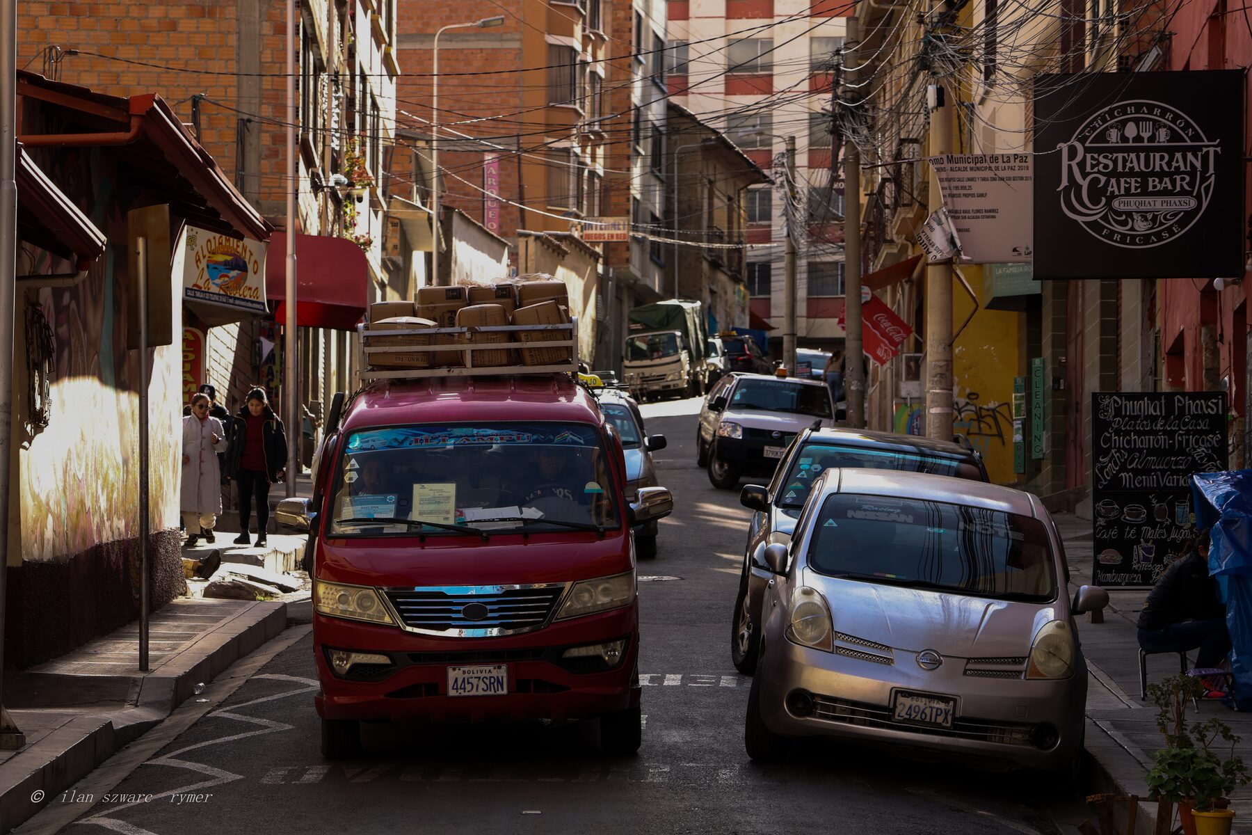 A loaded red minivan navigating a narrow city street